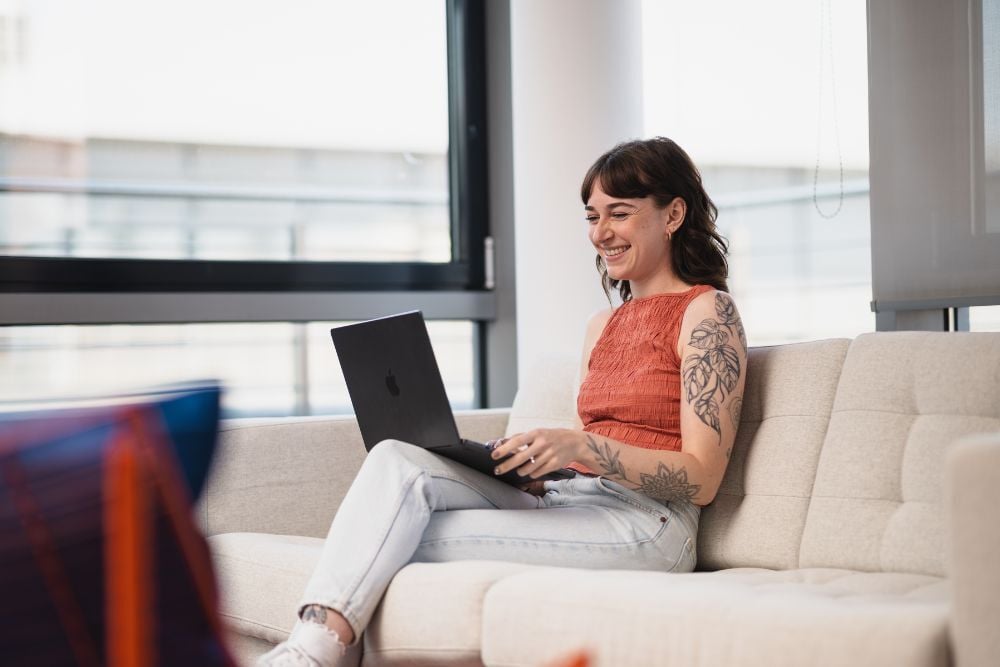 Person auf einer Couch sitzt und am Laptop arbeitet